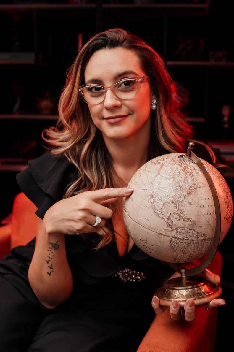Daniella Rolim em um estúdio escuro, apontando para um globo antigo